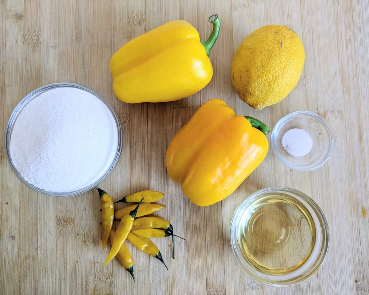 Lemon Drop chillies, yellow peppers, lemon, sugar, vinegar and salt arranged on a wooden board.