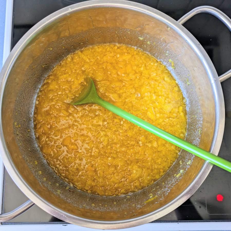 Chopped yellow peppers and chillies beginning to cook in a saucepan, with a green spatula resting in the mixture.