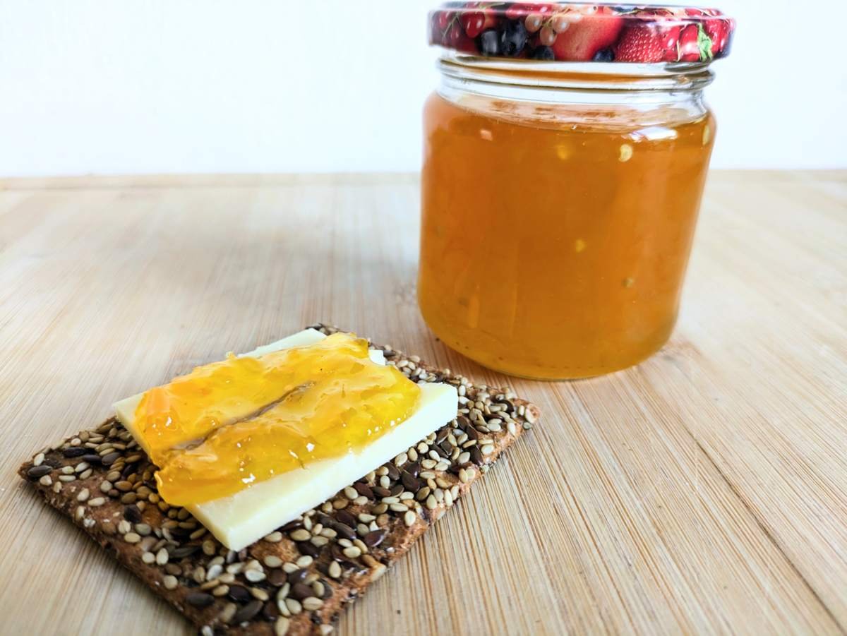 Seeded cracker topped with cheese and golden Lemon Drop chilli jam, with a jar of jam behind it.
