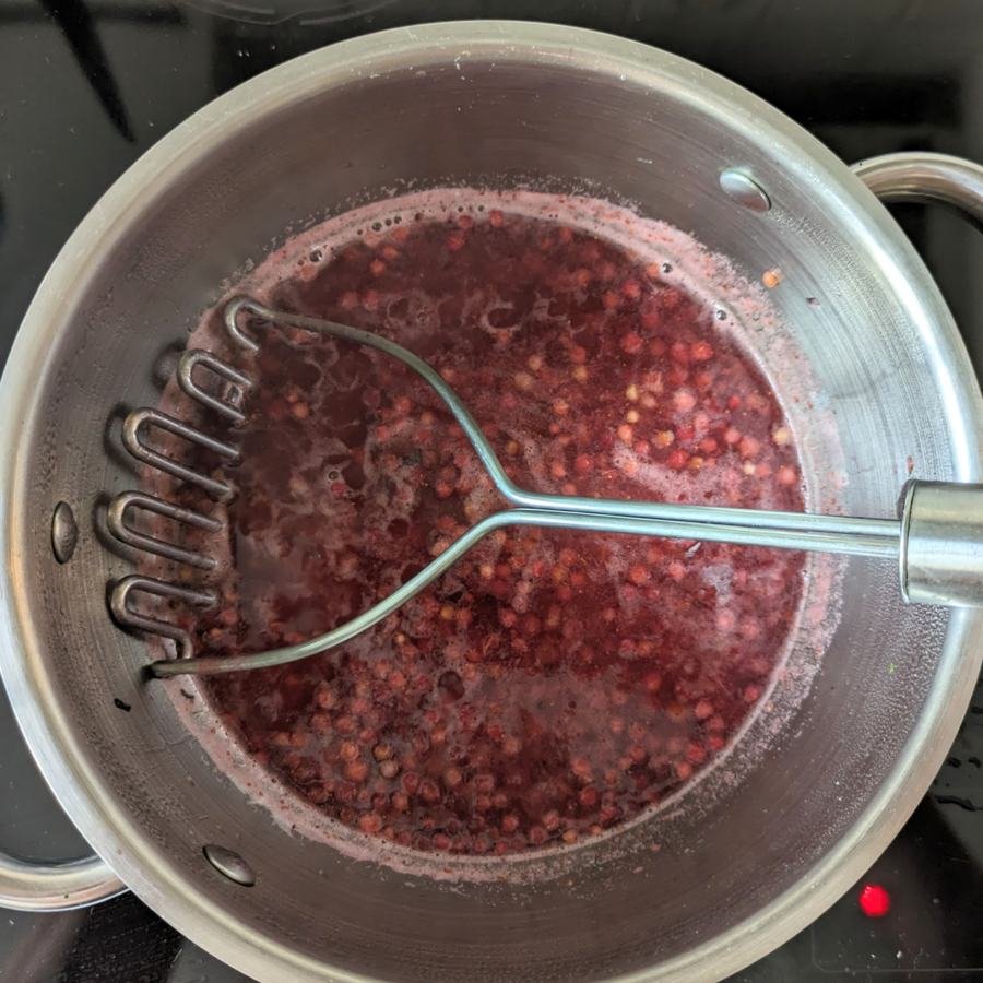 Lingonberries being mashed as they simmer in a saucepan.
