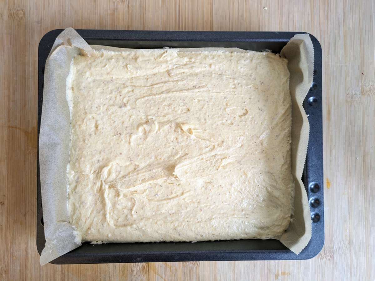 Cake batter spread evenly in a lined square baking tin before adding the plums and streusel.