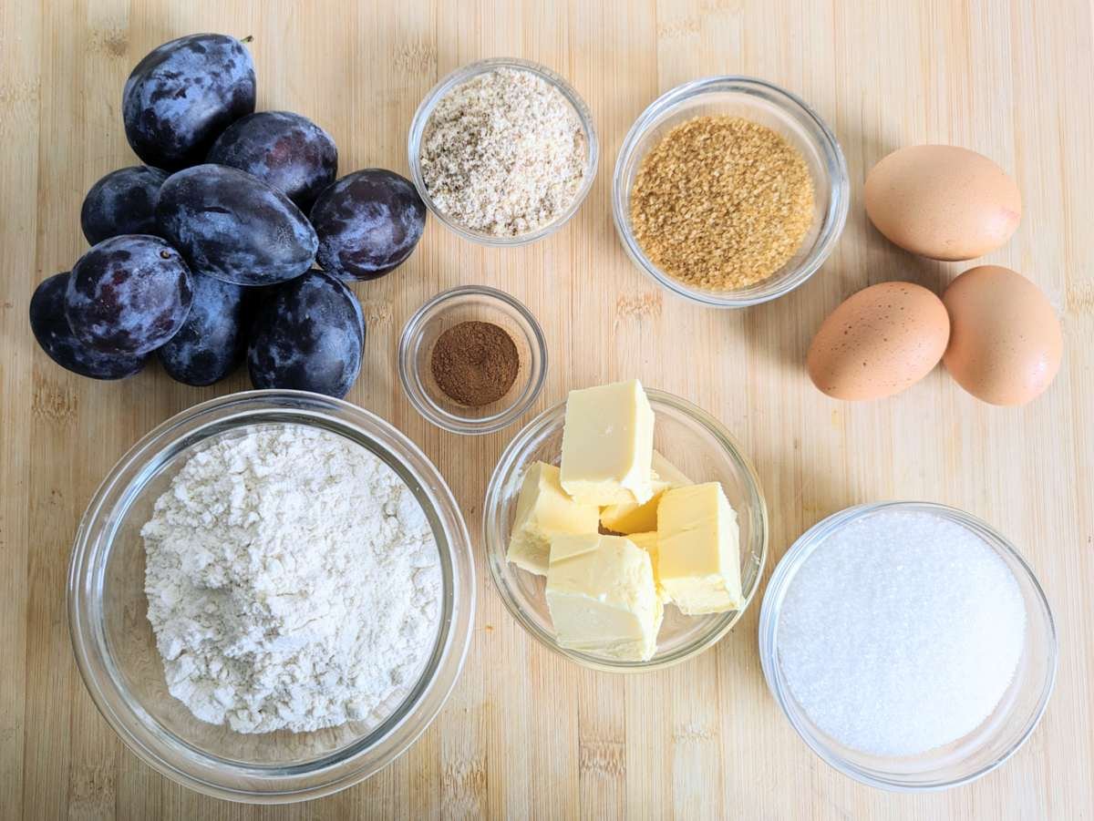 Ingredients for prune plum crumble cake, including fresh plums, flour, ground almonds, butter, eggs, sugar and cinnamon.