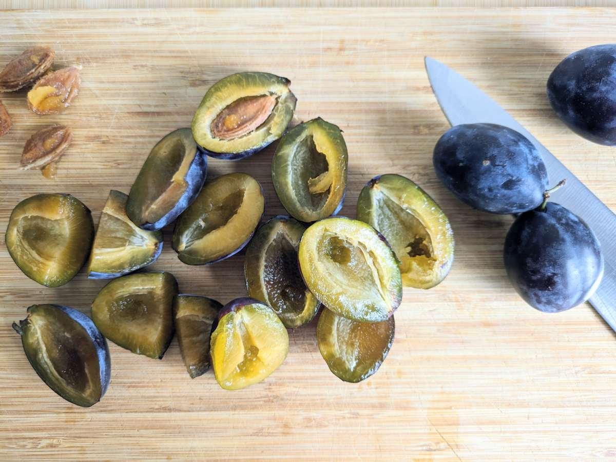 Halved and stoned prune plums on a wooden chopping board.