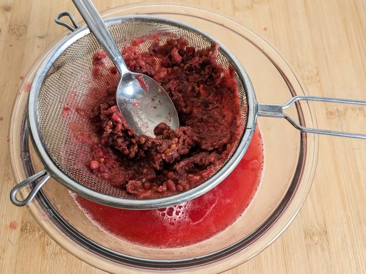 Cooked lingonberries being pressed through a sieve to extract the juice for syrup.