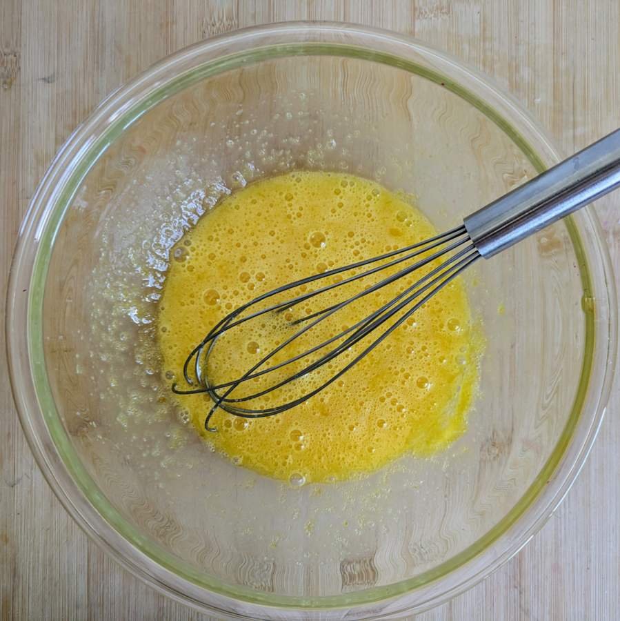 Eggs whisked together in a glass mixing bowl.
