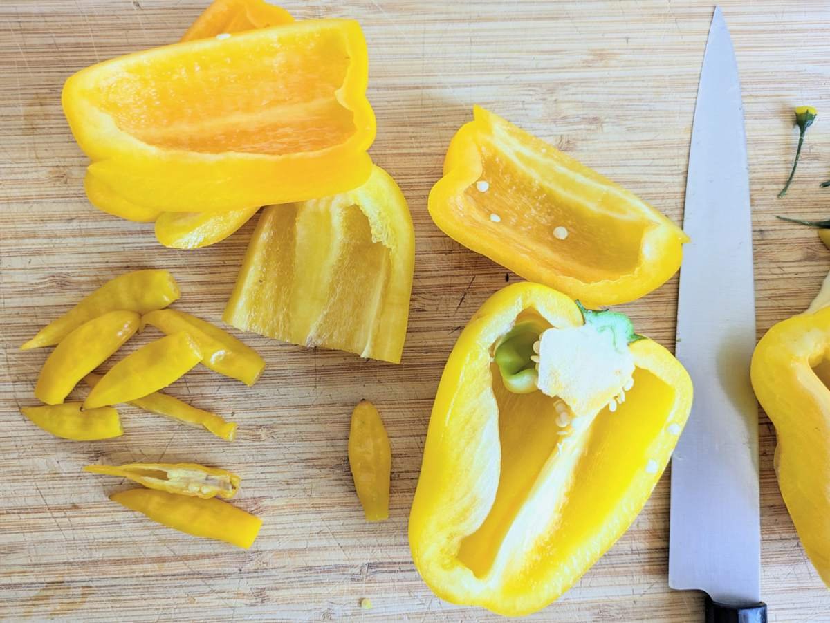Halved yellow bell peppers and a Lemon Drop chilli on a chopping board, with trimmed pieces beside a knife.