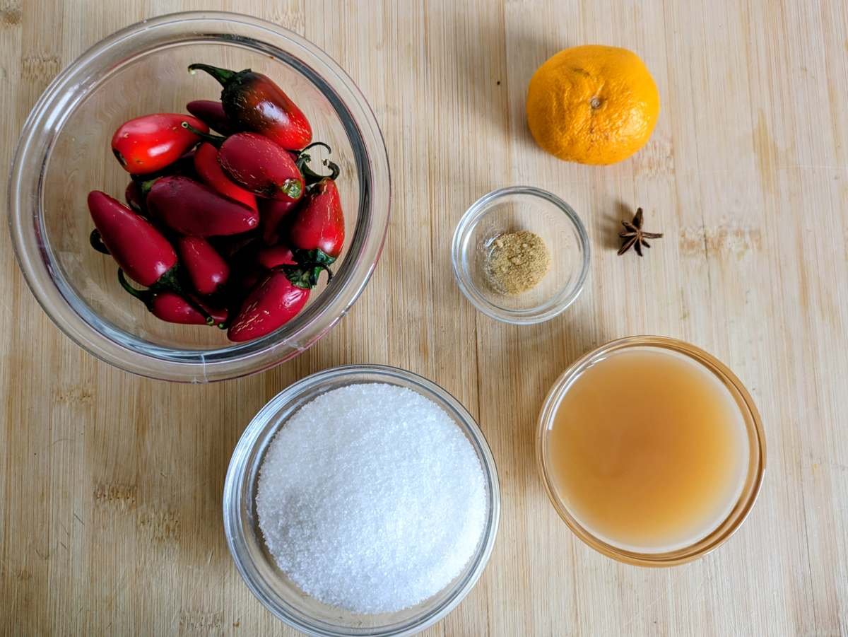 Ingredients for candied red jalapenos: red chillies, sugar, cider vinegar, citrus fruit, ground ginger and star anise on a wooden board.