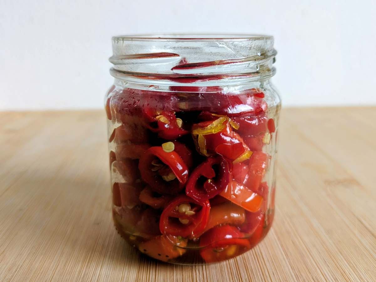 Cooked red chilli rings packed into an open glass jar on a wooden board.