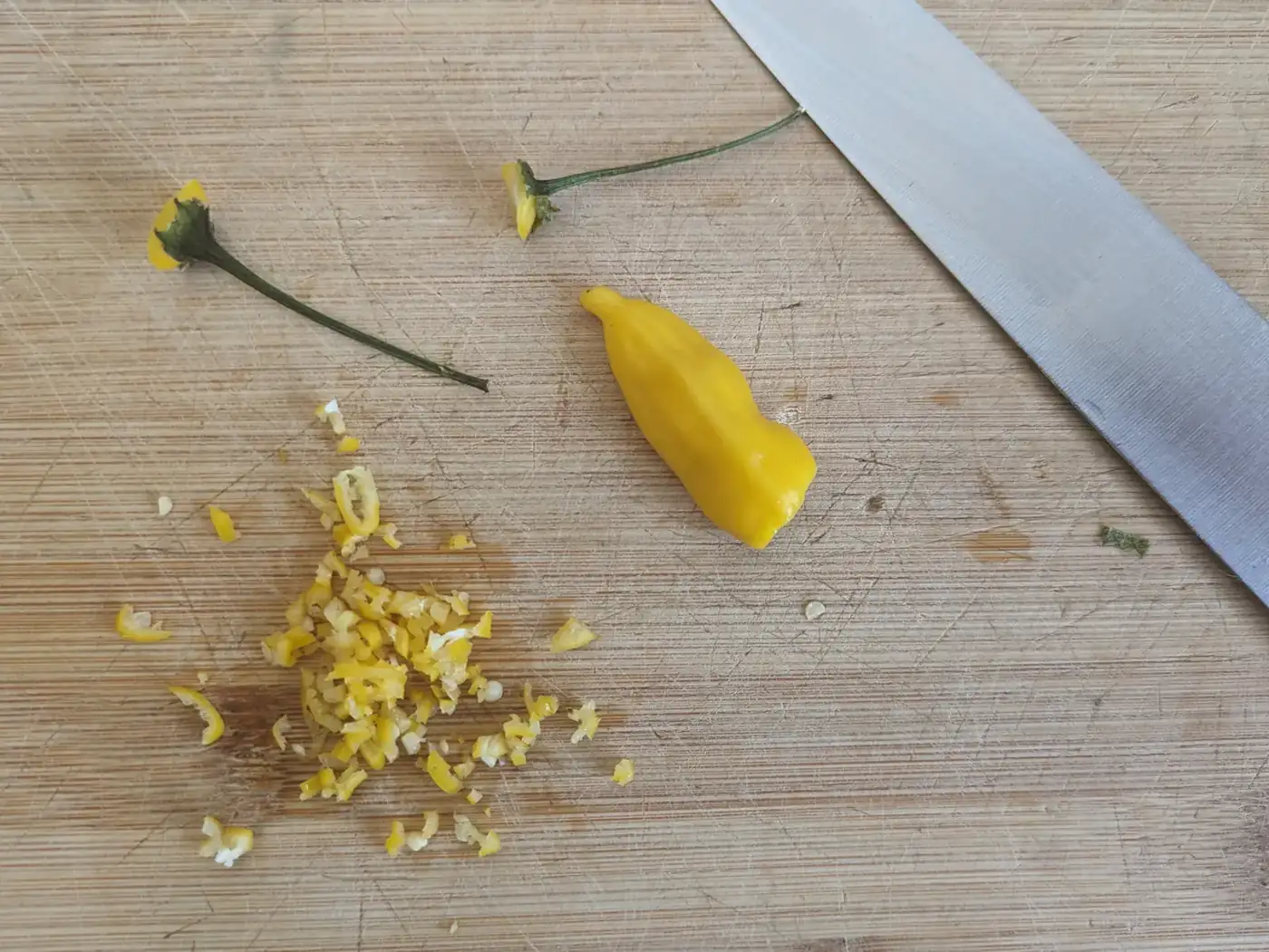 Whole and finely chopped yellow chillies on a wooden board beside a knife.