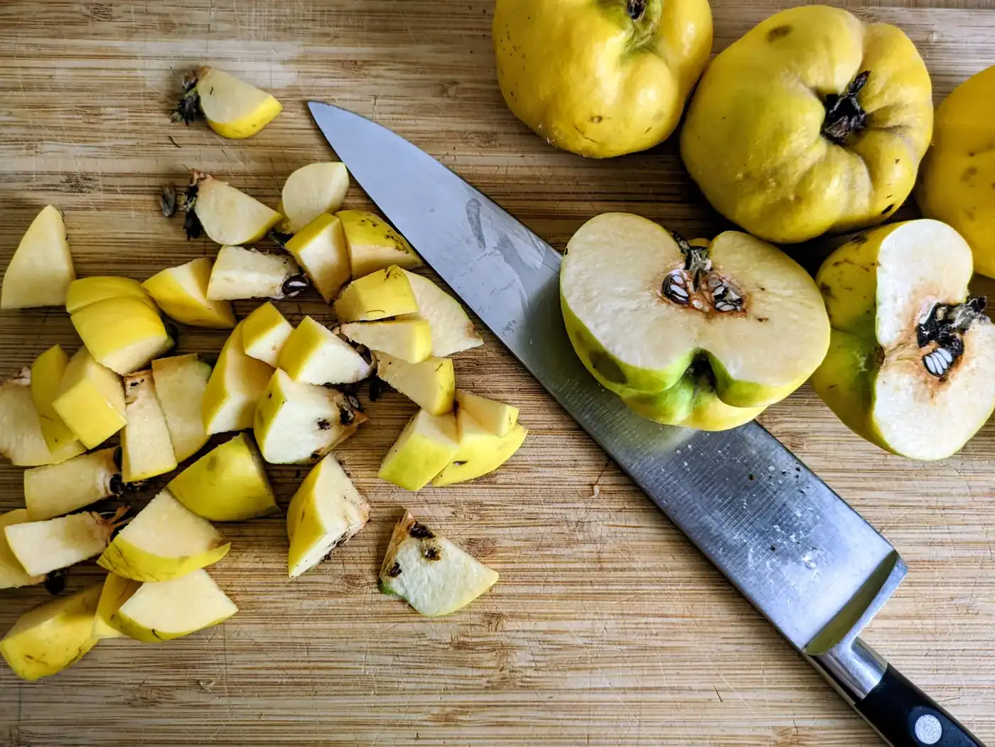 Chopped and halved quinces with skins and cores intact on a wooden chopping board.