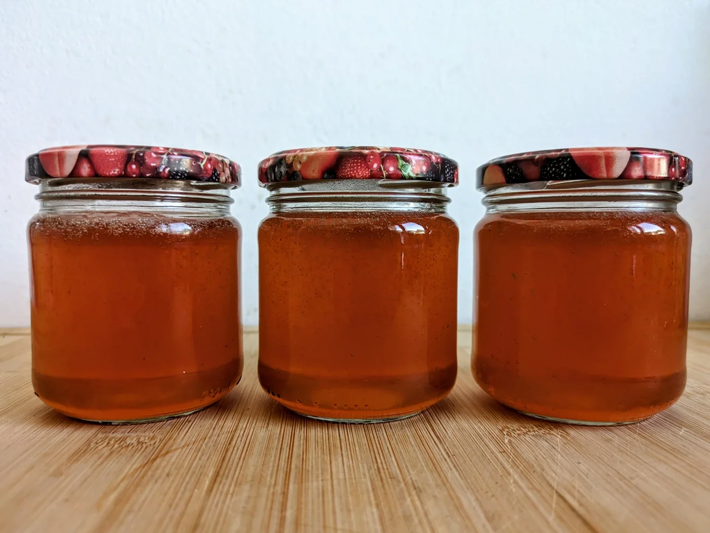 Three jars of amber quince jelly on a wooden board.