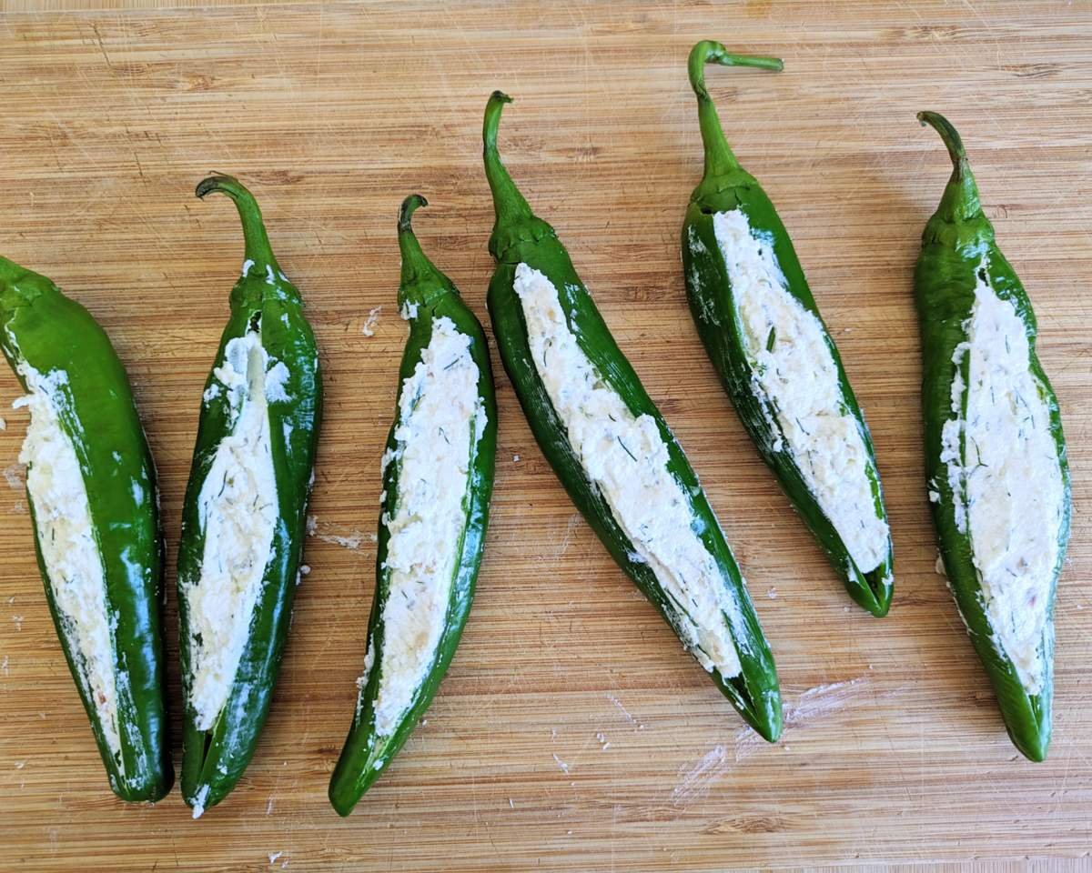 Six stuffed Anaheim peppers filled with feta, quark and herbs on a wooden chopping board before baking.