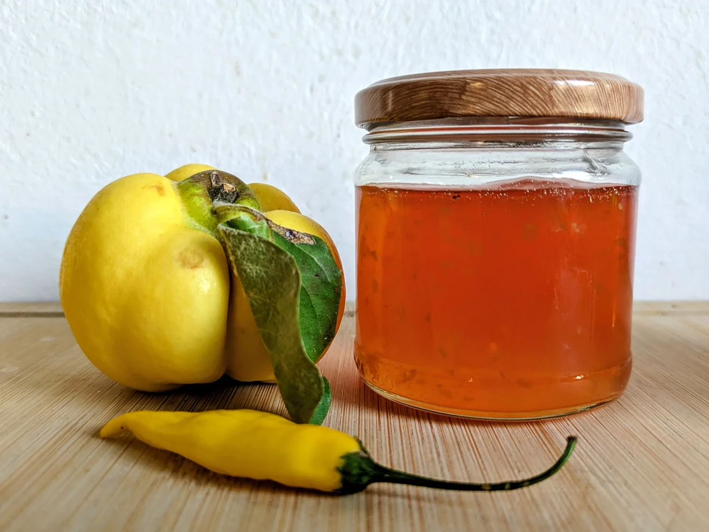Chilli variation of the quince jelly recipe in a jar beside a fresh quince and yellow chilli.