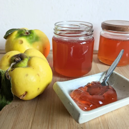 Quince jelly recipe with amber jelly in jars and a serving dish beside fresh quinces.