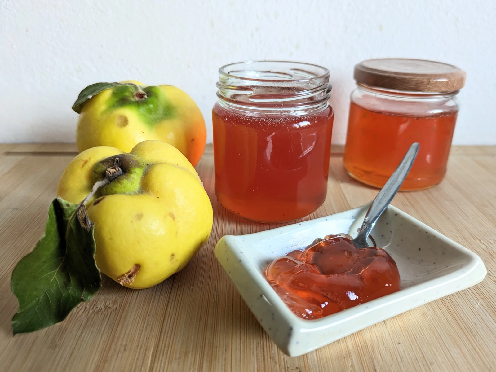 Quince jelly recipe with amber jelly in jars and a serving dish beside fresh quinces.