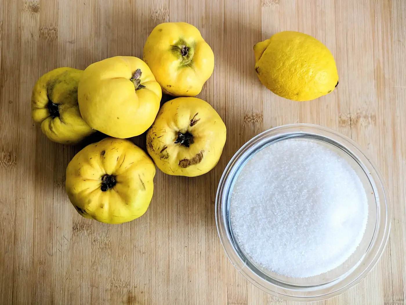 Fresh quinces, a lemon and granulated sugar on a wooden board ready for making quince jelly