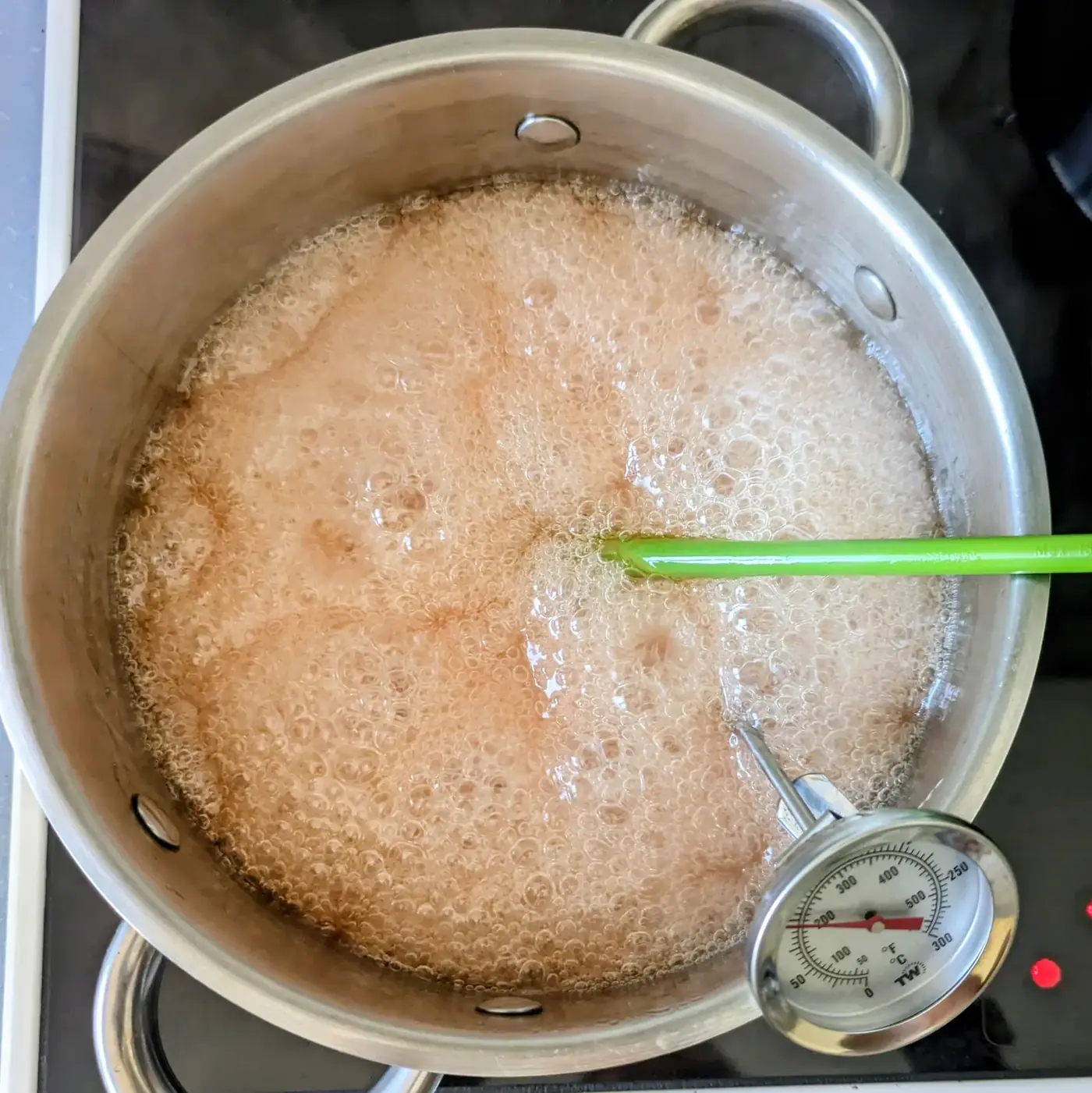 Jelly bubbling rapidly in a saucepan with a thermometer.