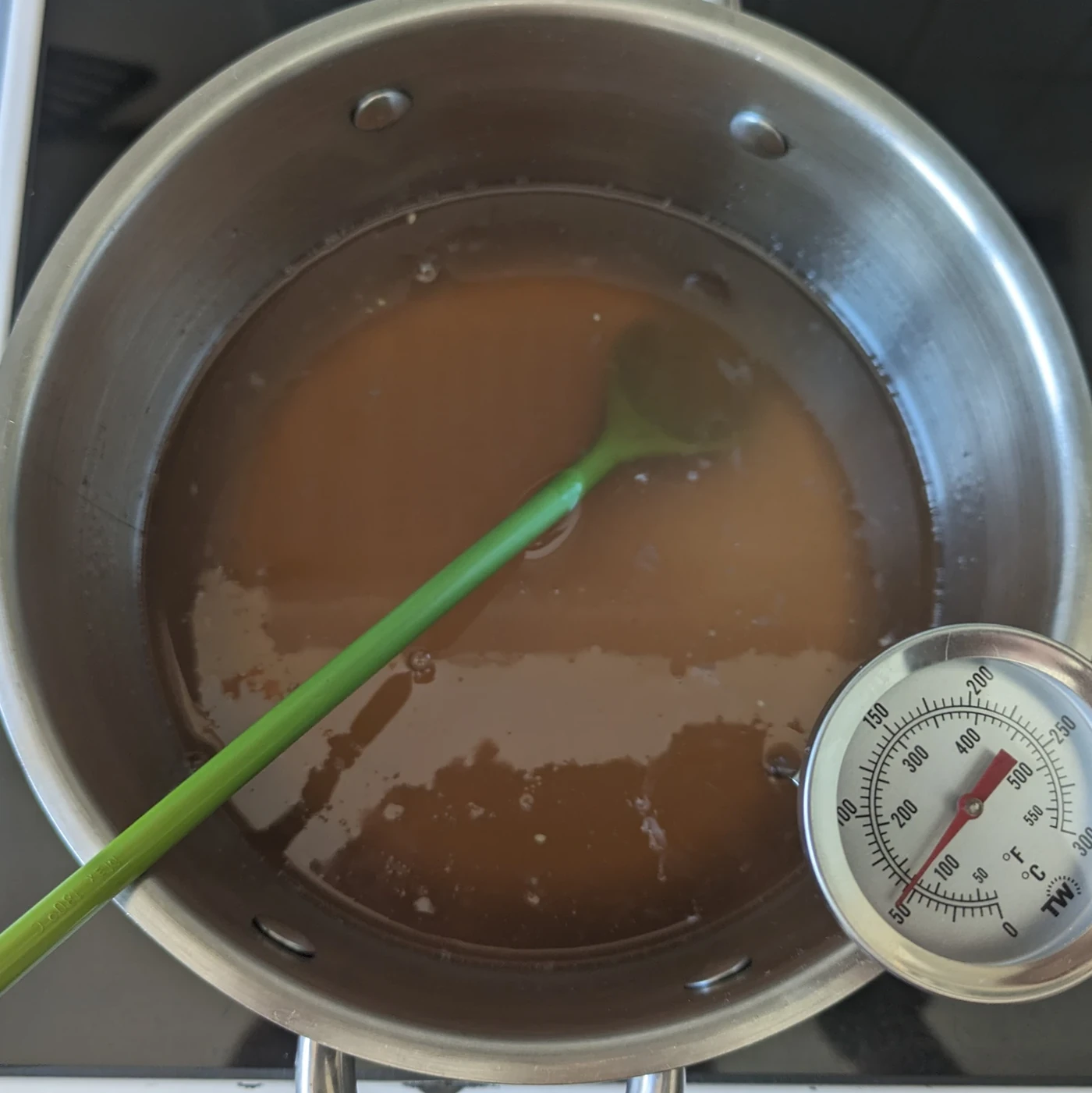 Strained quince syrup in a saucepan with a green spoon and thermometer.