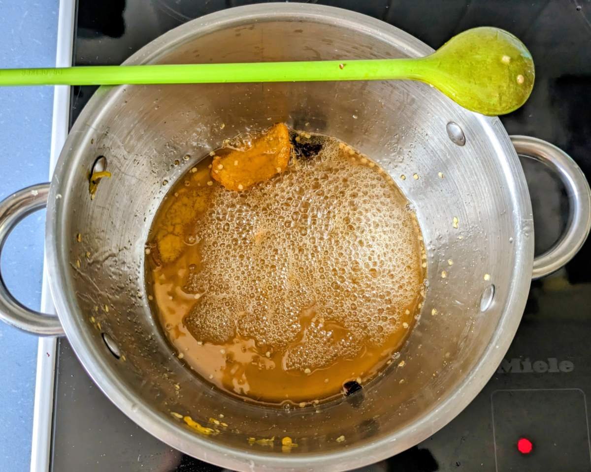 Golden syrup bubbling with citrus peel and star anise in a stainless steel pan.