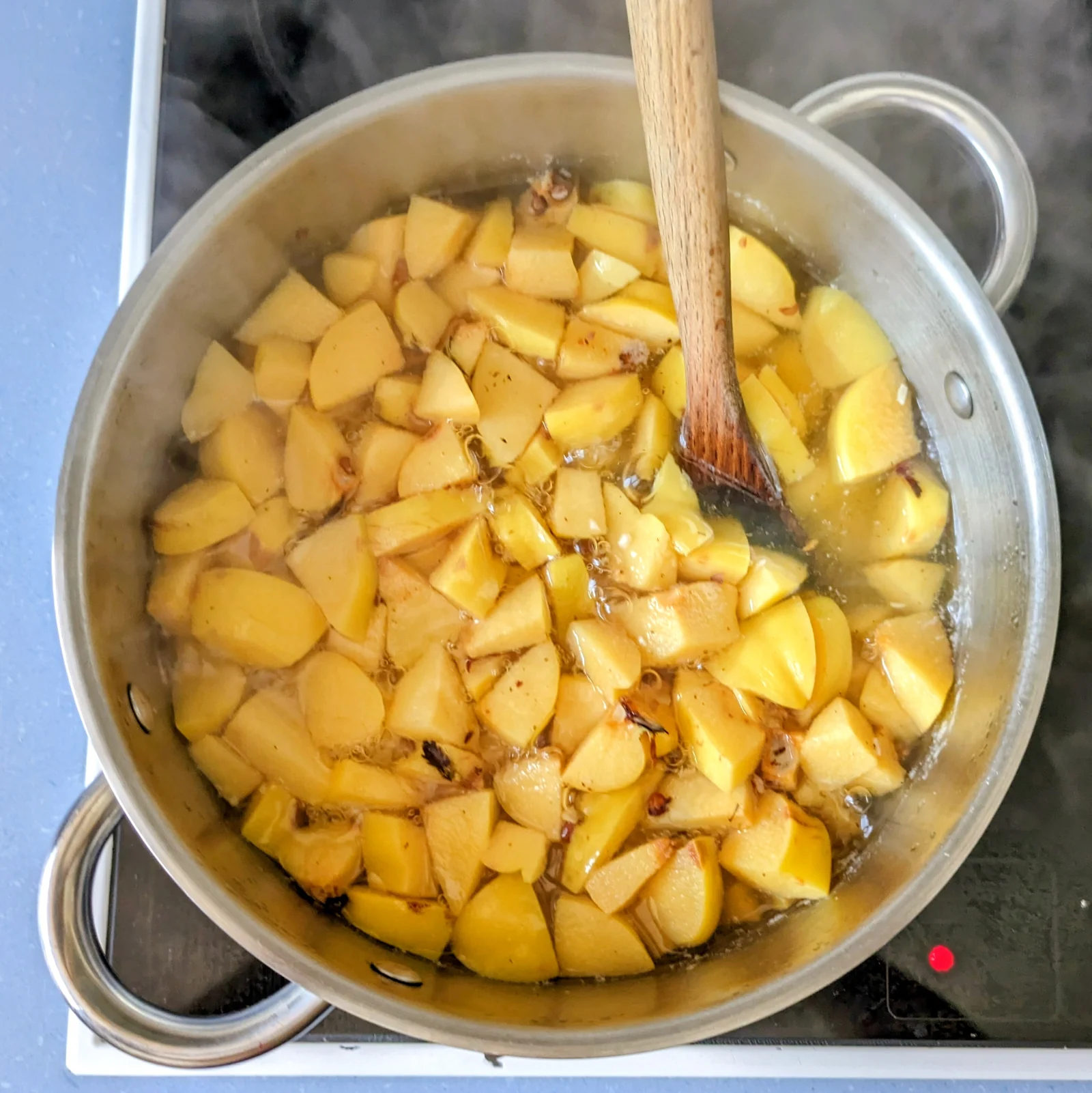 Chopped quinces simmering in water with a wooden spoon.