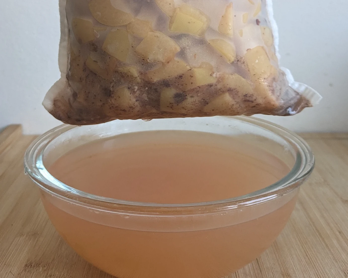 Cooked quinces draining through a jelly bag into a glass bowl.