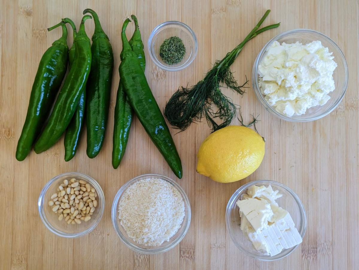 Ingredients for stuffed Anaheim peppers: green peppers, quark, feta, pine nuts, breadcrumbs, dill, dried oregano and lemon on a wooden board.