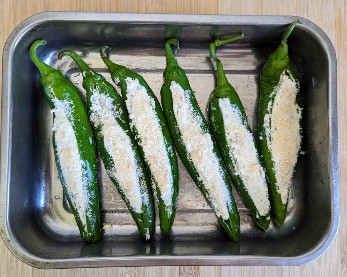 Six stuffed Anaheim peppers topped with breadcrumbs in a metal tin, ready to bake.