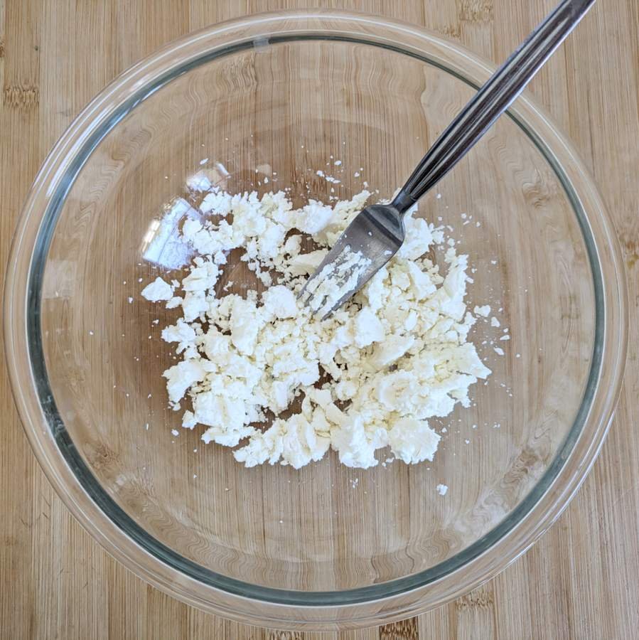 Crumbled feta and quark in a glass bowl with a fork.