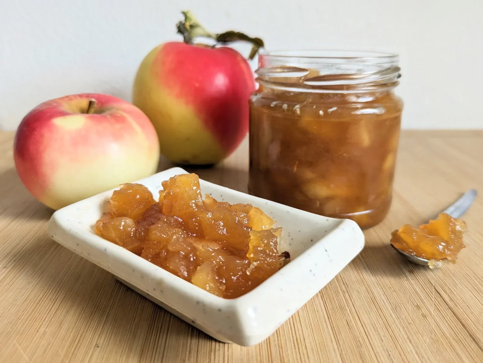 Toffee apple jam in a glass jar beside fresh apples and a small dish