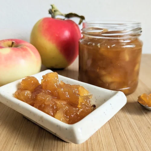 Toffee apple jam in a glass jar beside fresh apples and a small dish