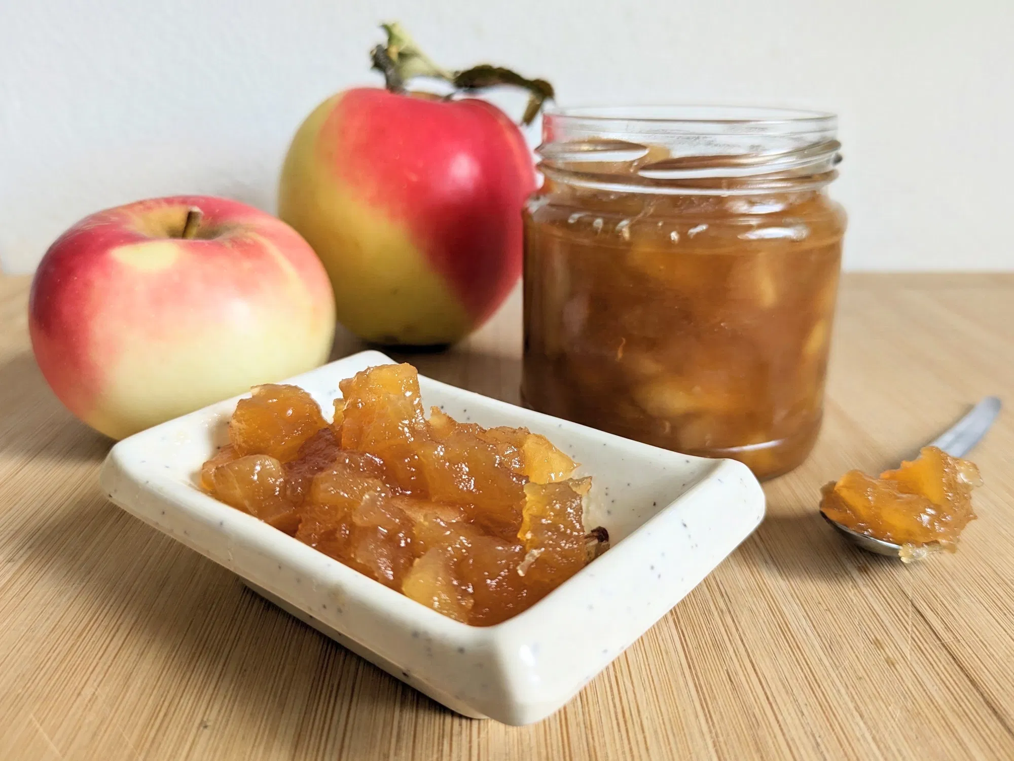 Toffee apple jam in a glass jar beside fresh apples and a small dish
