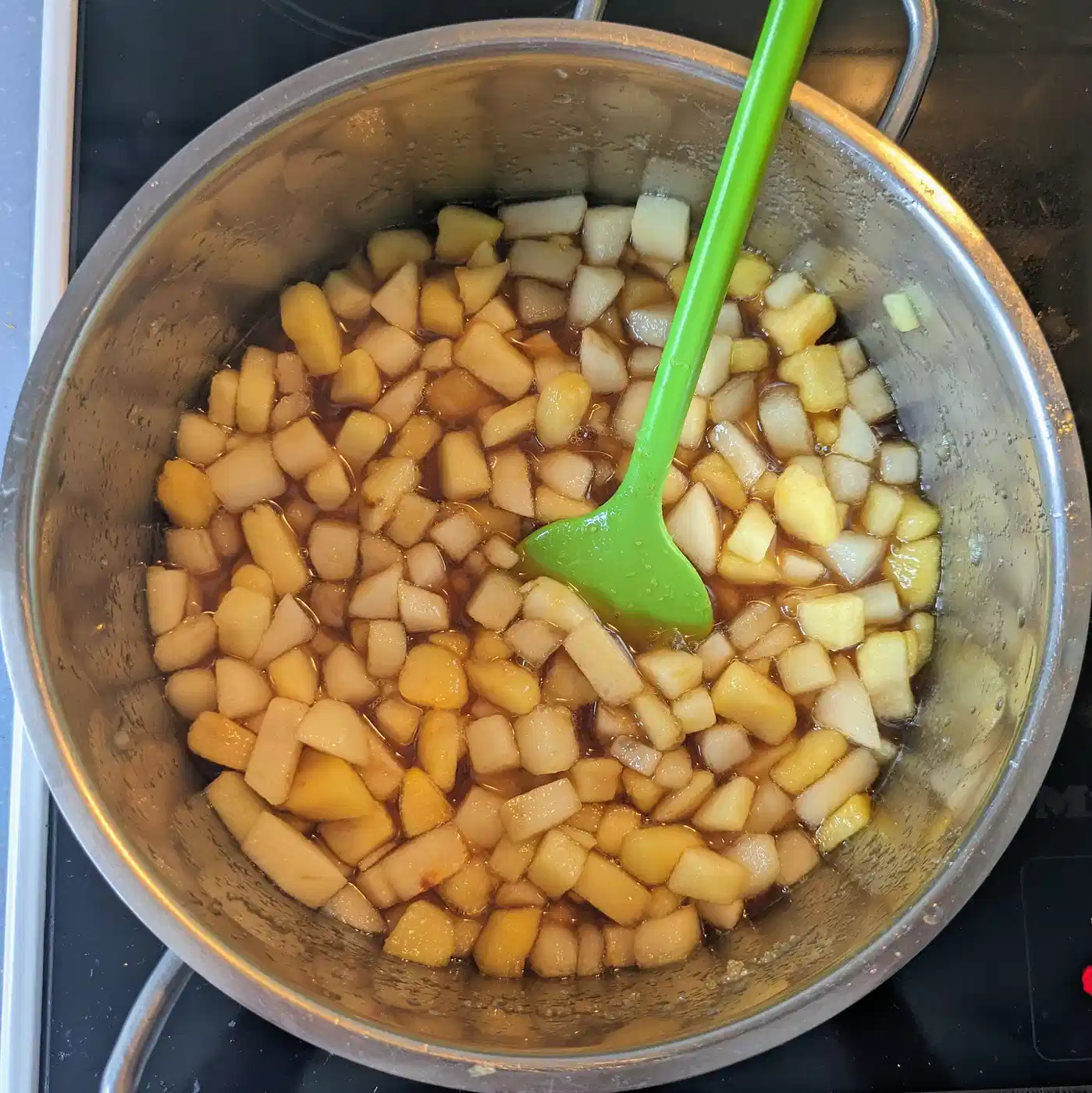 Caramel-coated apple pieces stirred with a green spatula